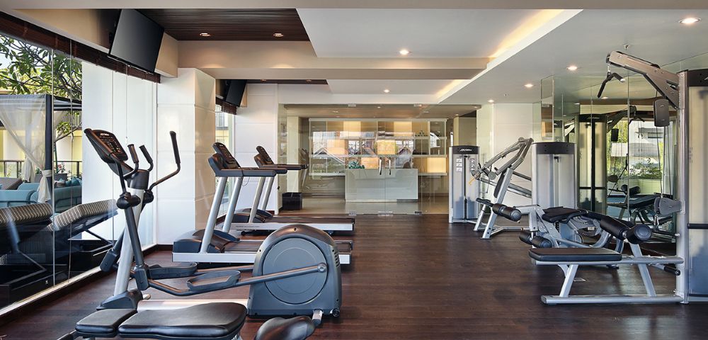 Modern gym interior with treadmills, exercise bikes, and weight machines on dark wooden floors. Bright lighting creates a clean, inviting atmosphere.