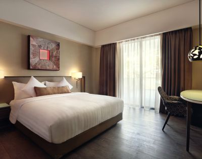 Modern hotel room with a large bed, white linens, and decorative pillows. Soft lighting and abstract art create a cozy, welcoming atmosphere.