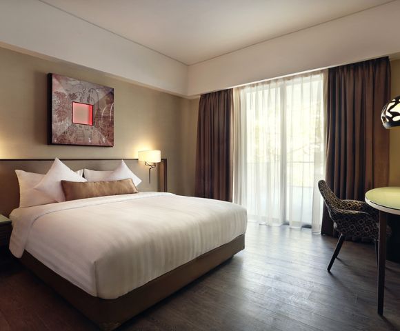 Modern hotel room with a large bed, white linens, and decorative pillows. Soft lighting and abstract art create a cozy, welcoming atmosphere.