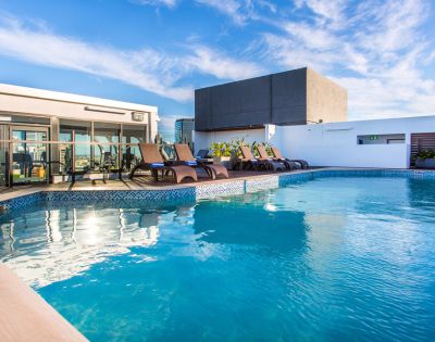 Rooftop pool with clear blue water and surrounding lounge chairs under a bright sky. Modern building backdrop, evoking a tranquil, luxurious vibe.