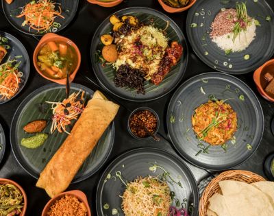 A variety of colorful Indian dishes on black plates, including dosa, rice, vegetables, and curries, creating a vibrant and appetizing spread.