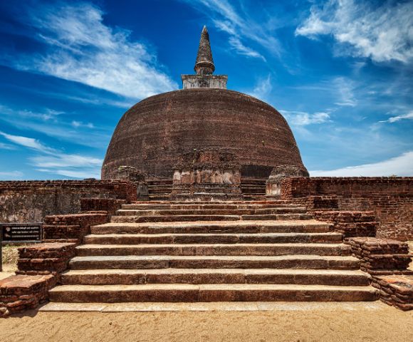 Ancient brick stupa with a domed structure and stone steps leading up to it, under a bright blue sky at Polonnaruwa in Sri Lanka.