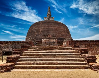 Ancient brick stupa with a domed structure and stone steps leading up to it, under a bright blue sky at Polonnaruwa in Sri Lanka.