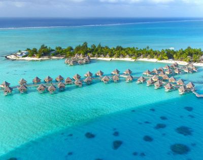 Aerial view of a tropical island with overwater bungalows and lush greenery surrounded by clear turquoise ocean, conveying a serene and idyllic atmosphere.