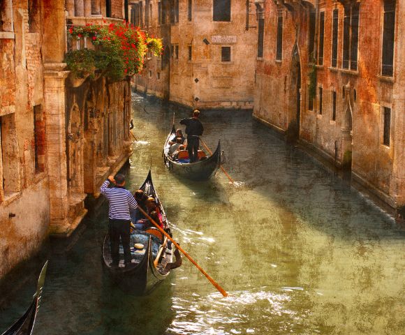 Two gondolas navigate a narrow Venetian canal, guided by gondoliers. Sunlight bathes the aged, warm-toned buildings, creating a serene, nostalgic ambiance.