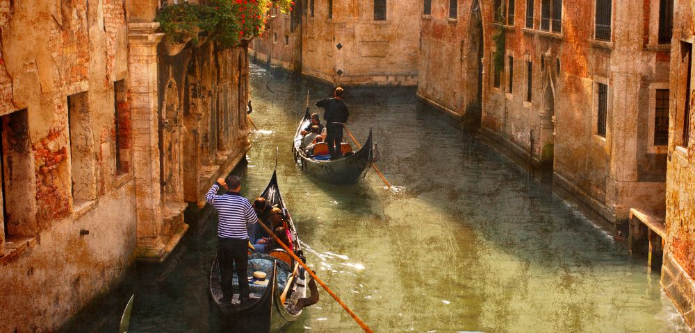 Two gondolas navigate a narrow Venetian canal, guided by gondoliers. Sunlight bathes the aged, warm-toned buildings, creating a serene, nostalgic ambiance.