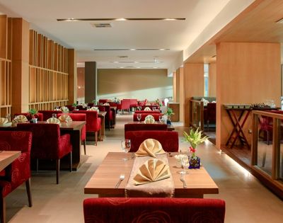 Cozy restaurant interior featuring red upholstered chairs, neatly set tables with folded napkins, wooden accents, dim lighting, and a welcoming ambiance.