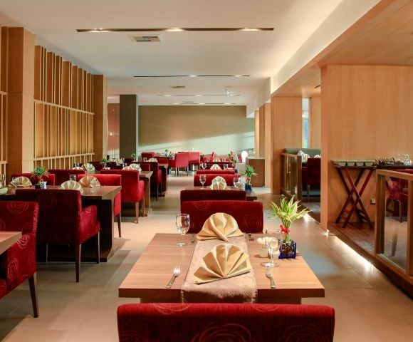 Cozy restaurant interior featuring red upholstered chairs, neatly set tables with folded napkins, wooden accents, dim lighting, and a welcoming ambiance.