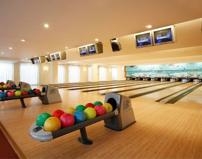 Bright bowling alley with multiple lanes, colorful bowling balls on racks, and score screens overhead. Spacious, inviting atmosphere, ready for play.