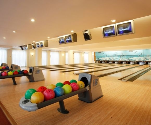 Bright bowling alley with multiple lanes, colorful bowling balls on racks, and score screens overhead. Spacious, inviting atmosphere, ready for play.