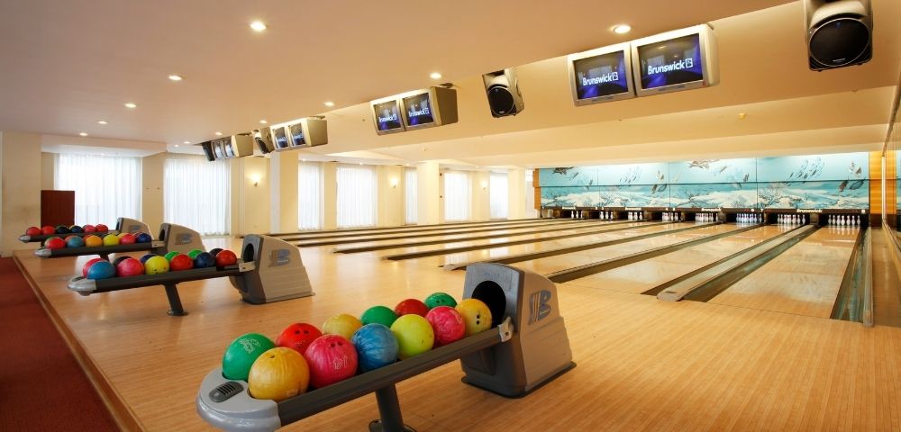 Bright bowling alley with multiple lanes, colorful bowling balls on racks, and score screens overhead. Spacious, inviting atmosphere, ready for play.