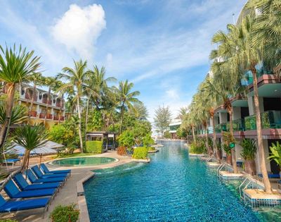 Resort pool scene with blue loungers, flanked by lush palm trees and modern buildings. Bright, sunny day with a serene and inviting atmosphere.