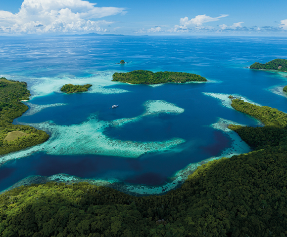 Aerial view of a tropical seascape with lush green islands surrounded by turquoise water and coral reefs. A small boat is visible, evoking serenity.