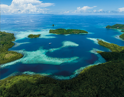 Aerial view of a tropical seascape with lush green islands surrounded by turquoise water and coral reefs. A small boat is visible, evoking serenity.