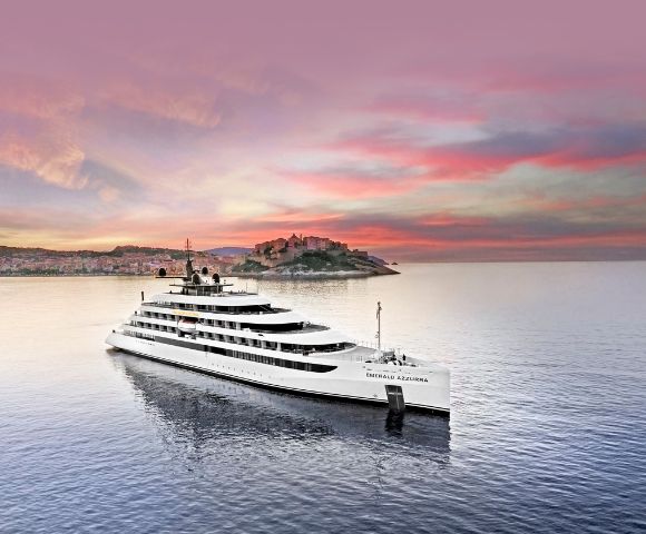 The luxury yacht Emerald Azzurra cruising on tranquil seas at sunset, with a Mediterranean coastal town and pastel sky in the background.
