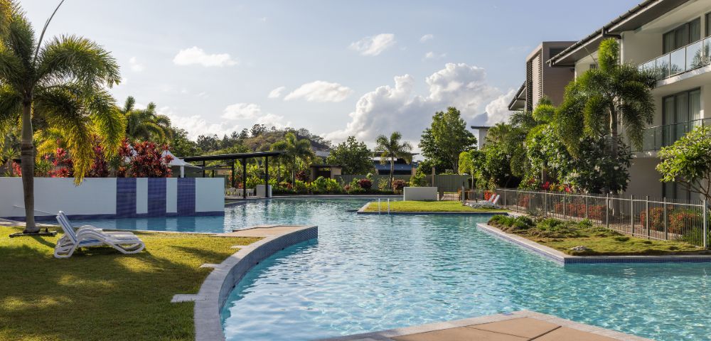 A serene outdoor pool surrounded by lush greenery and palm trees under a clear blue sky, conveying a peaceful, inviting, and tropical atmosphere.