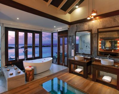 Luxurious bathroom with ocean views, a freestanding tub, and double sinks on wooden vanities. Warm lighting and candles create a serene atmosphere.