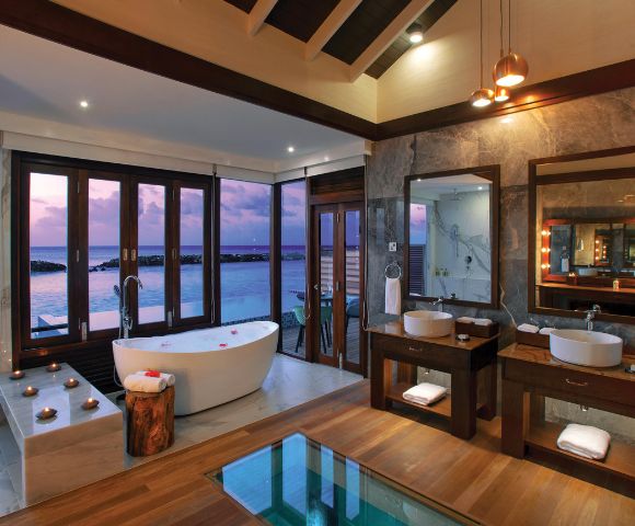 Luxurious bathroom with ocean views, a freestanding tub, and double sinks on wooden vanities. Warm lighting and candles create a serene atmosphere.