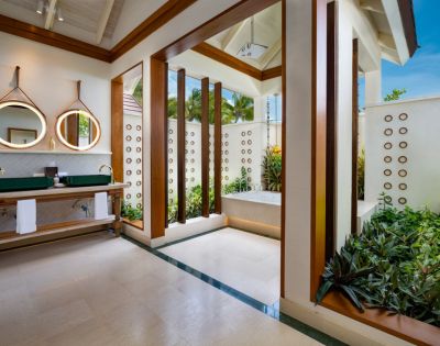 Bright, modern bathroom with open ceiling and lush plants. Features a tub, green countertop with dual sinks, and circular mirrors, creating a serene, spa-like ambiance.
