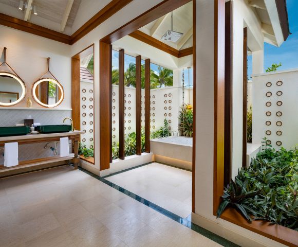 Bright, modern bathroom with open ceiling and lush plants. Features a tub, green countertop with dual sinks, and circular mirrors, creating a serene, spa-like ambiance.