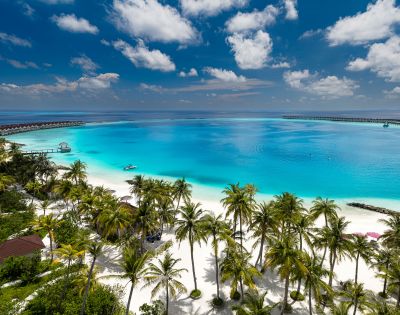 Tropical beach scene with turquoise ocean, white sand, and lush palm trees under a vibrant blue sky with scattered clouds. Peaceful and inviting atmosphere.