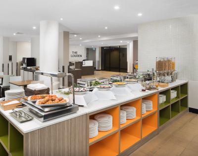 Buffet area with a modern design, featuring a variety of breakfast items like pastries, cereals, and juices. Bright, clean, and inviting atmosphere.