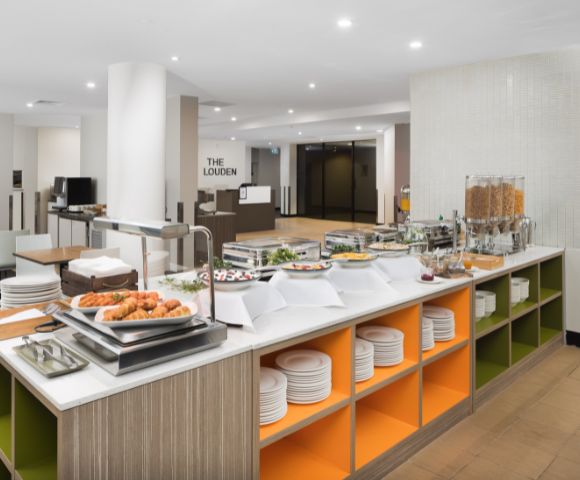 Buffet area with a modern design, featuring a variety of breakfast items like pastries, cereals, and juices. Bright, clean, and inviting atmosphere.