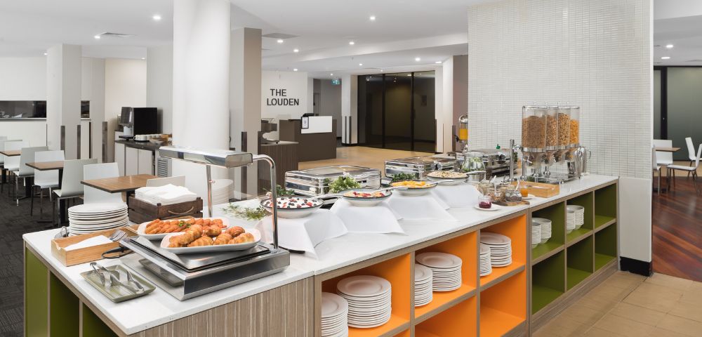 Buffet area with a modern design, featuring a variety of breakfast items like pastries, cereals, and juices. Bright, clean, and inviting atmosphere.