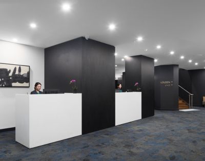 Modern reception area with two sleek white desks, dark walls, and soft lighting. Two receptionists are working, creating an efficient and welcoming atmosphere.