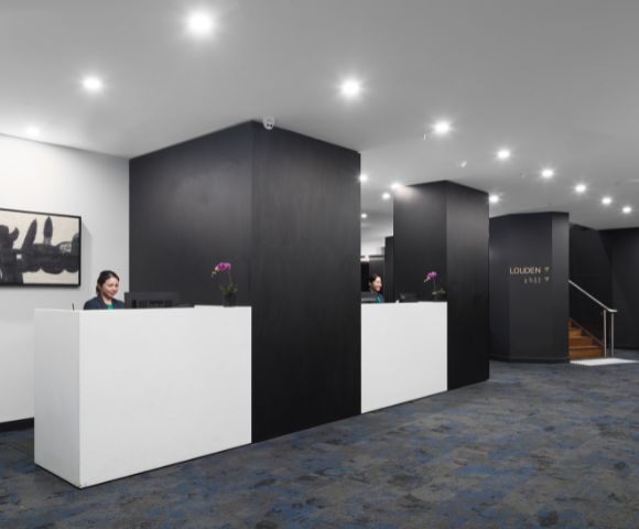 Modern reception area with two sleek white desks, dark walls, and soft lighting. Two receptionists are working, creating an efficient and welcoming atmosphere.
