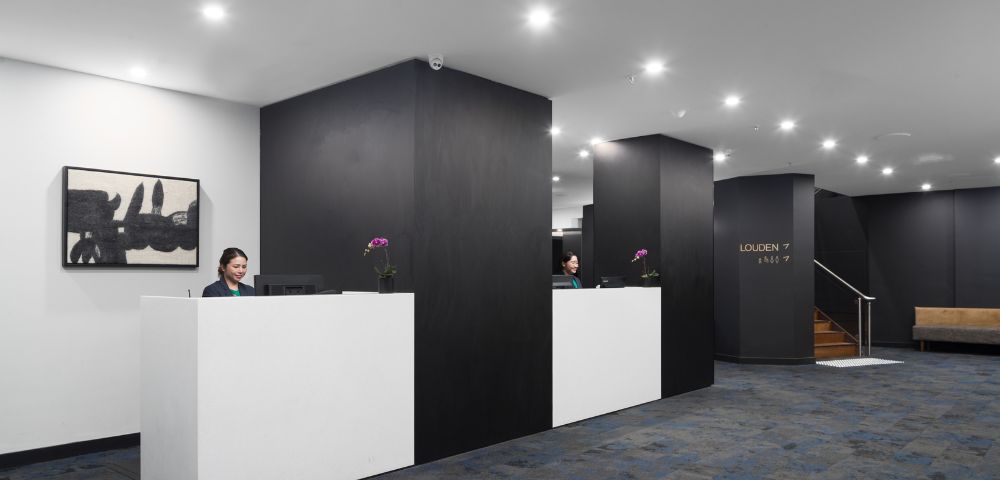 Modern reception area with two sleek white desks, dark walls, and soft lighting. Two receptionists are working, creating an efficient and welcoming atmosphere.