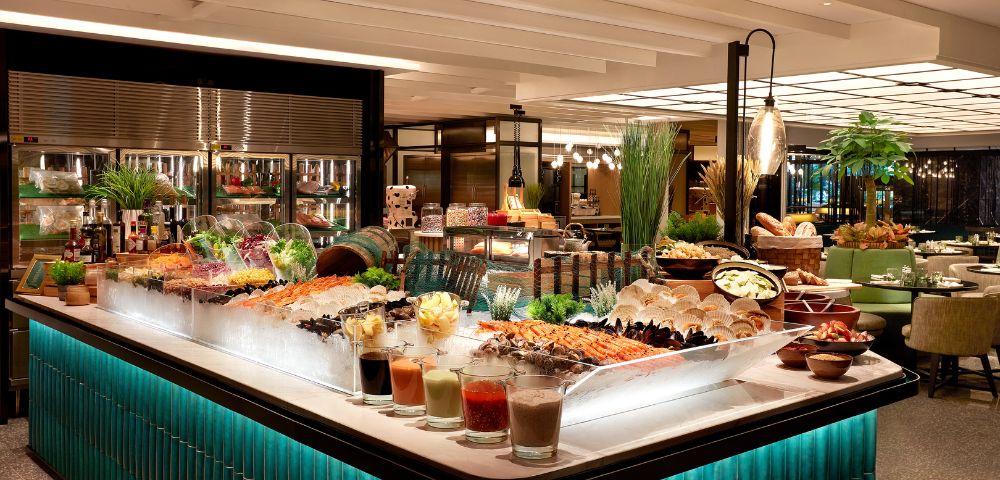 Luxurious buffet with a variety of seafood on ice, colorful salads, and garnishes. Elegant lighting and green-tiled counters create a refined atmosphere.