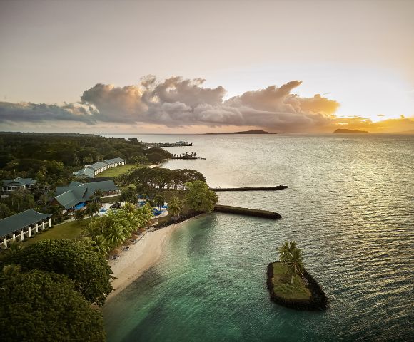 Aerial view of a serene coastal landscape at sunset. Calm ocean with gentle waves, lush greenery, and a sandy beach evoke a tranquil and idyllic mood.