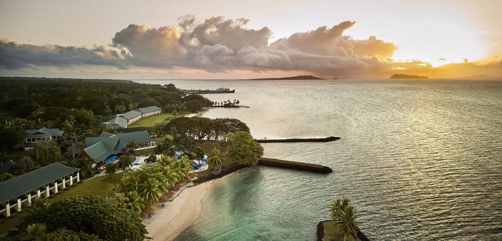 Aerial view of a serene coastal landscape at sunset. Calm ocean with gentle waves, lush greenery, and a sandy beach evoke a tranquil and idyllic mood.
