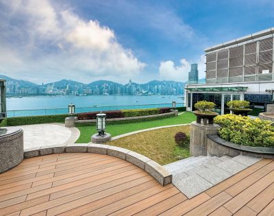 Rooftop terrace overlooking a calm harbor, with distant city skyline. Wooden decking and manicured greenery create a serene, inviting atmosphere.