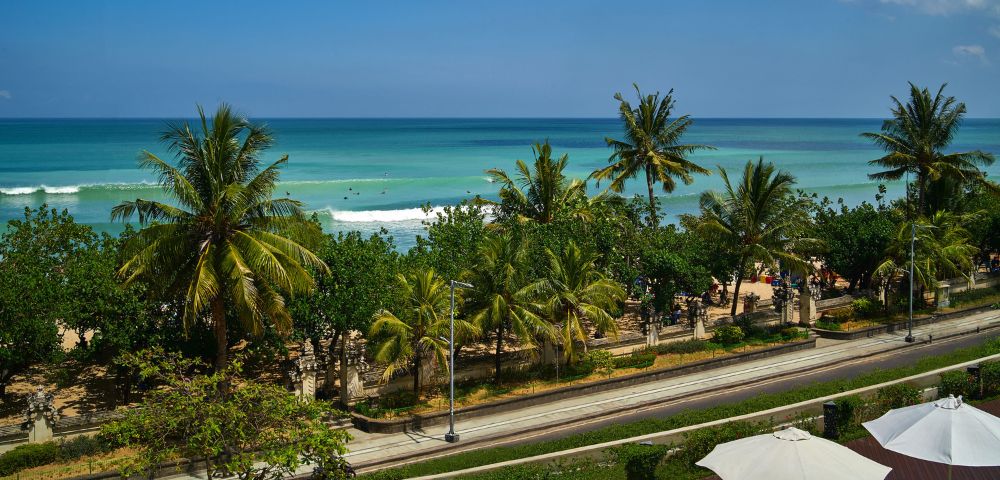 A scenic view of the beach and ocean from a balcony, with waves gently lapping at the shore.