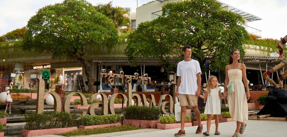 A family strolls together in front of a bustling shopping mall, enjoying their day out.