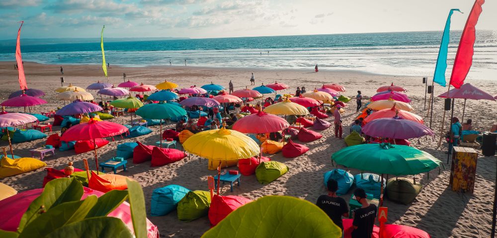 Colourful umbrellas dot the sandy beach, creating a vibrant scene under the bright sun.