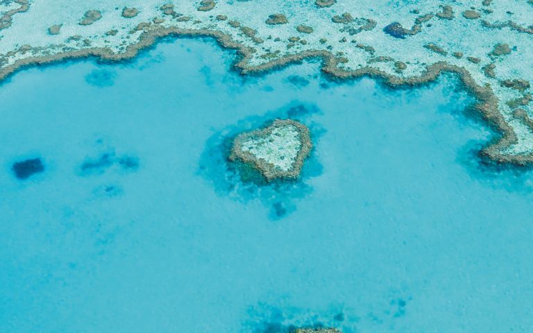 Aerial view of a turquoise ocean with a heart-shaped coral reef. The vibrant blue water contrasts with the intricate reef patterns, creating a serene atmosphere.