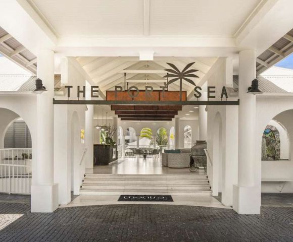 Entrance of a coastal resort with arched white walls and a high ceiling. Sign reads 