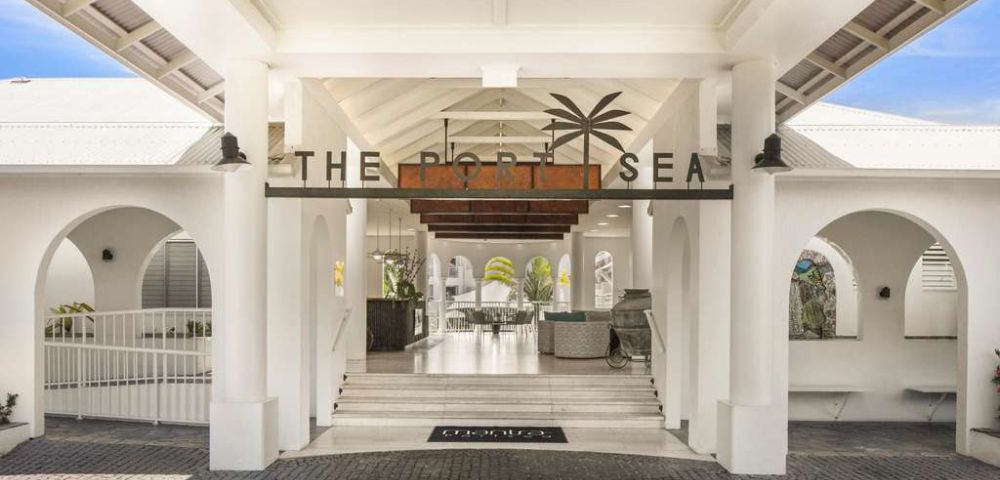 Entrance of a coastal resort with arched white walls and a high ceiling. Sign reads 