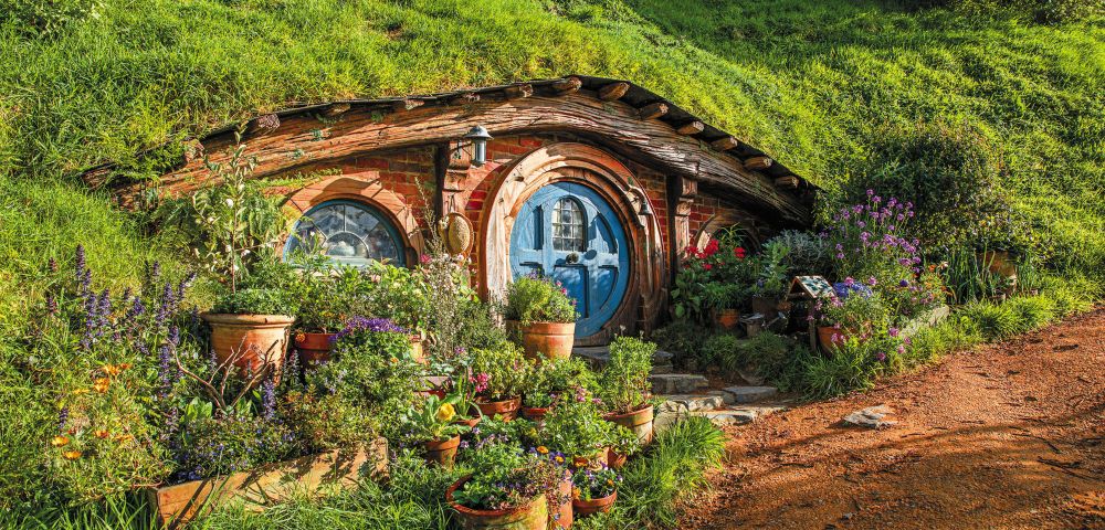 Charming hobbit house with a round blue door set into a grassy hillside. Surrounded by vibrant flowers and plants, evoking a whimsical, tranquil mood.