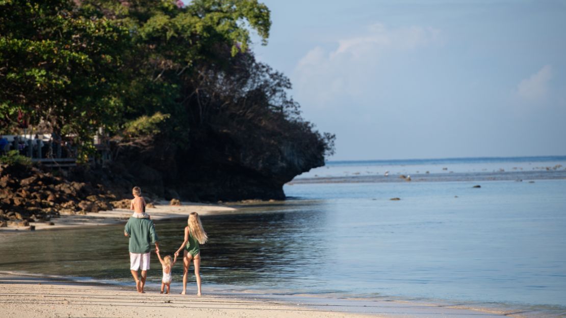 Family walking along the sandy beach with green trees in the background