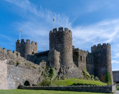 Ancient stone castle with round towers and battlements under a vibrant blue sky. Flags atop the towers add a sense of history and grandeur.