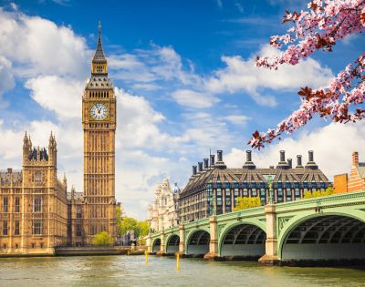 View of Big Ben and the Houses of Parliament in London on a sunny day with a clear blue sky. Cherry blossoms frame the scene in the foreground.