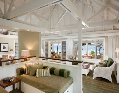 Airy coastal living room with white wicker furniture and green accents. Large windows offer a serene ocean view, conveying relaxation and tranquility.