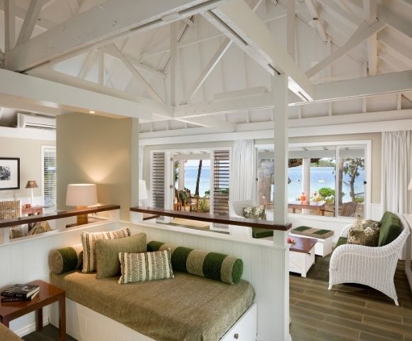 Airy coastal living room with white wicker furniture and green accents. Large windows offer a serene ocean view, conveying relaxation and tranquility.