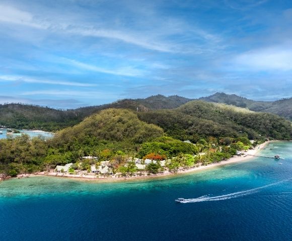 Aerial view of a lush, tropical island surrounded by turquoise ocean. Sandy beaches and distant hills evoke a serene and inviting paradise atmosphere.