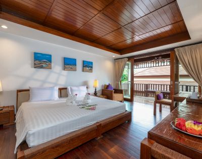 Elegant hotel room featuring a large bed with white linens, wooden furniture, artwork on the wall, and a balcony with open curtains letting in natural light.