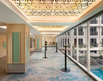 Spacious hallway with patterned ceiling and large windows overlooking a courtyard. Blue-green carpet and minimalist décor create a serene, modern ambiance.